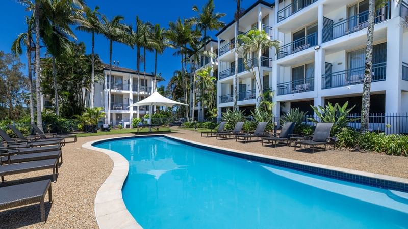 The Billabong Pool surrounded by lounge chairs and lush greenery at Mercure Gold Coast Resort in Carrara.