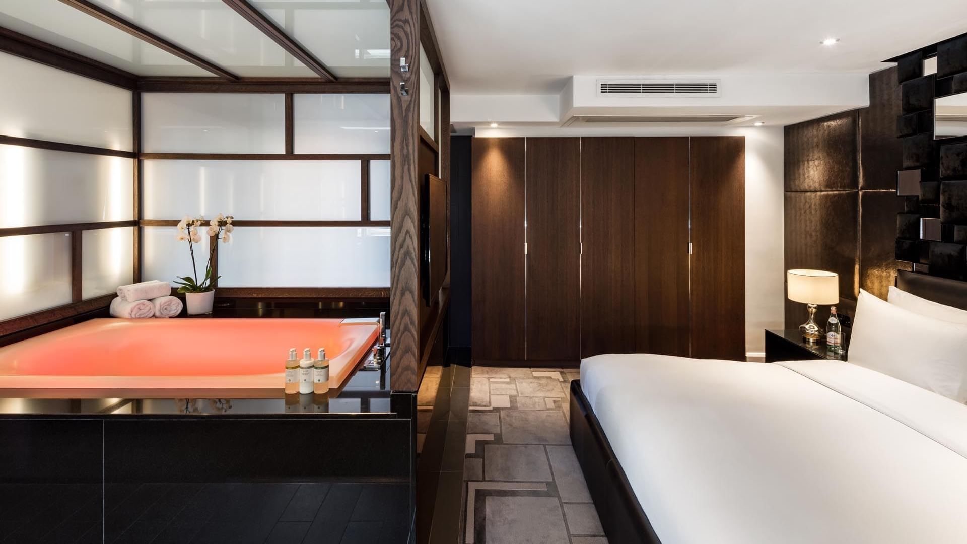 The Ebony Suite at The May Fair Hotel, London, with a large white bed beside an illuminated sunken bathtub