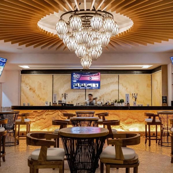 Elegant interior with a grand chandelier and TV in Suspiro Bar at Marquis Los Cabos Resort