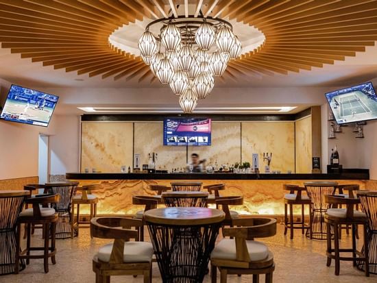 Elegant interior with a grand chandelier and TV in Suspiro Bar at Marquis Los Cabos Resort