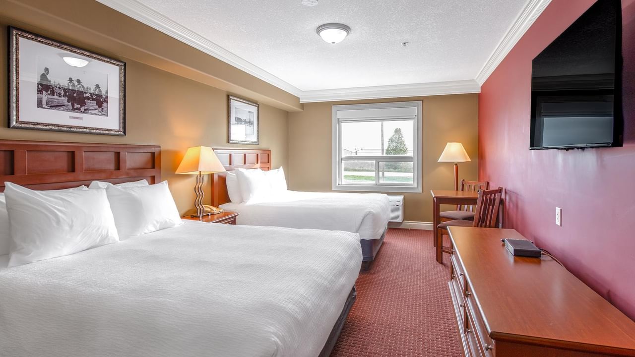Double room with two beds, wooden headboards, beige walls, pink accent wall, and wall-mounted TV at Coast Edson Hotel.