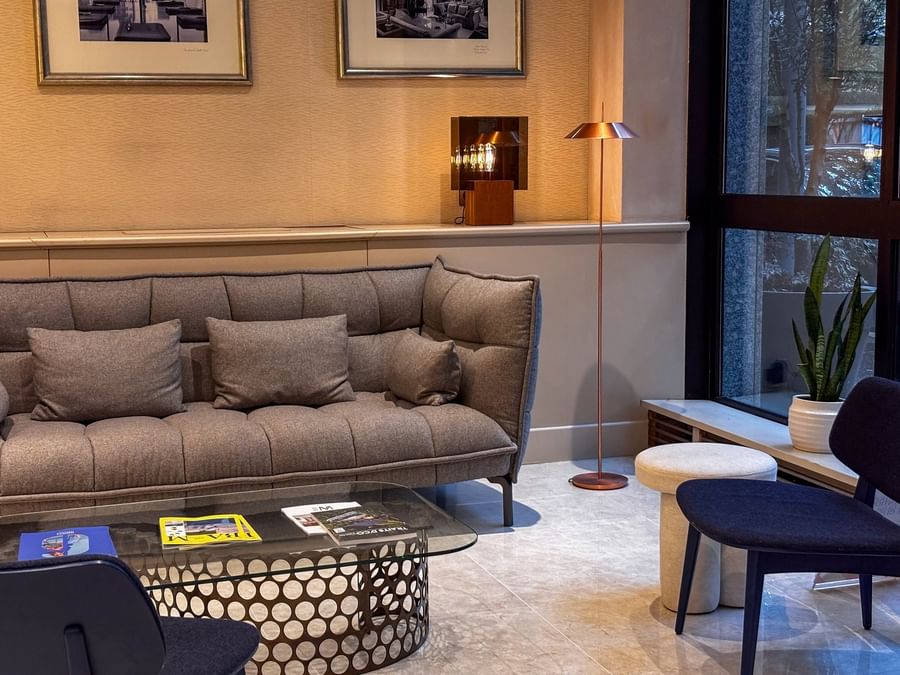 Cozy modern lounge with a gray sofa, a glass coffee table with magazines, and a floor lamp at Warwick Reine Astrid - Lyon