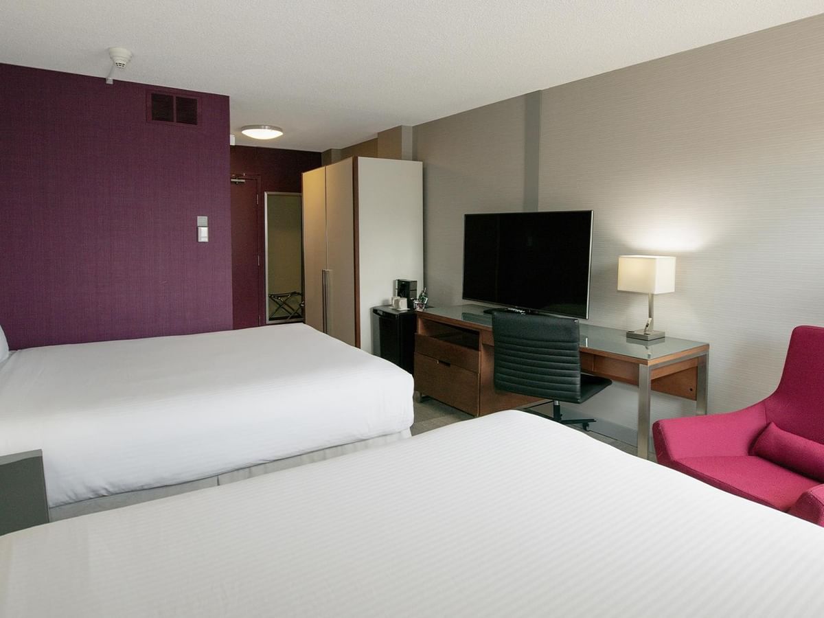 Coast Two Queens room with two queen beds, purple accent wall, flat-screen TV, and pink chair at Coast Prince George Hotel