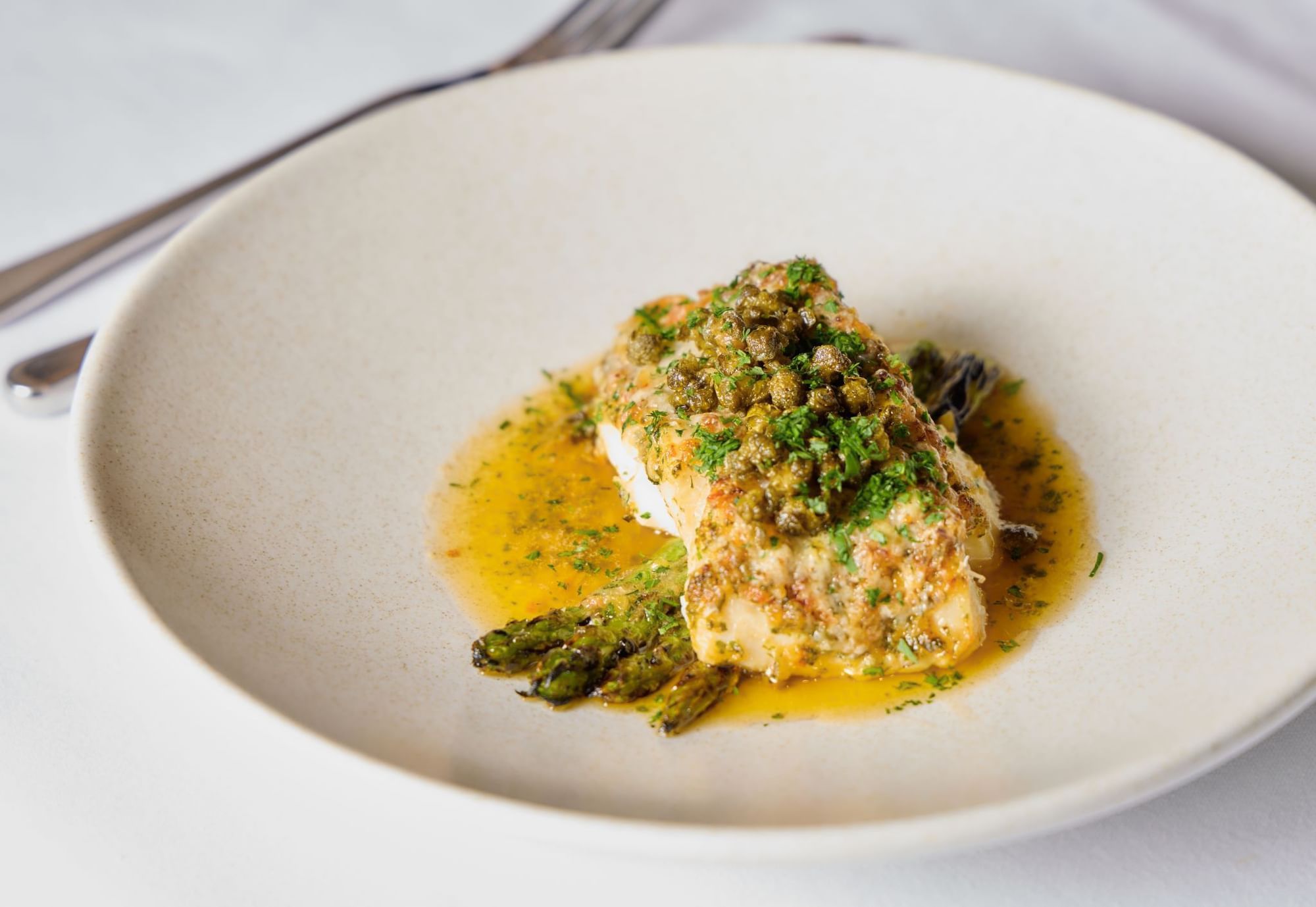 A beautifully plated fish dish with capers and asparagus in a rich sauce served in Whitcomb's Terrace at The Londoner Hotel