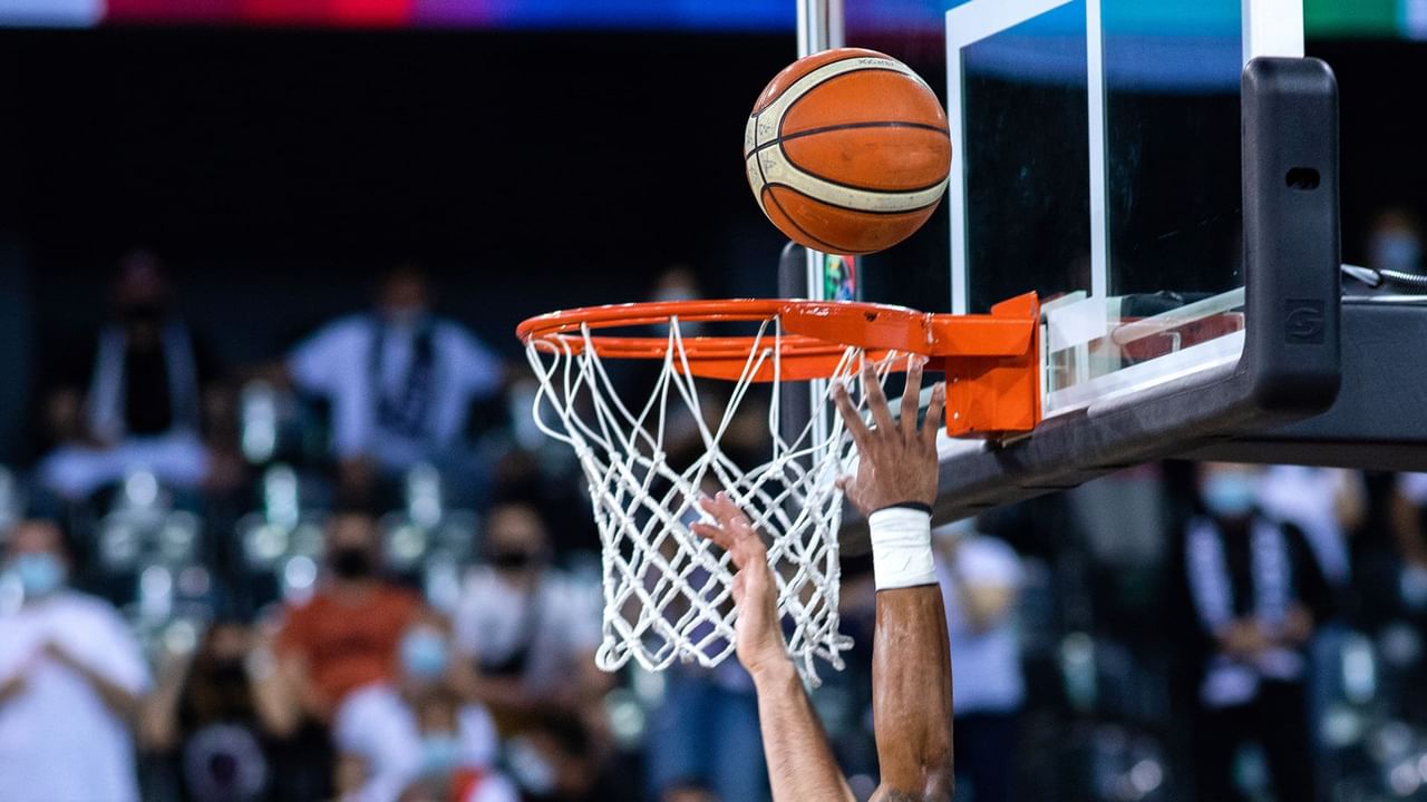 Basketball player slams a basketball into the hoop in front of an audience