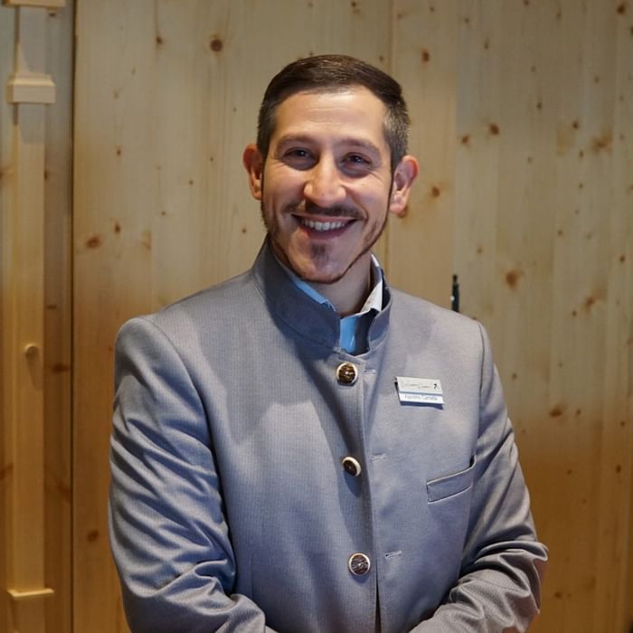 Lächelnder Mann in elegantem grauen Anzug vor hölzerner Wand bei Falkensteiner Hotel Montafon