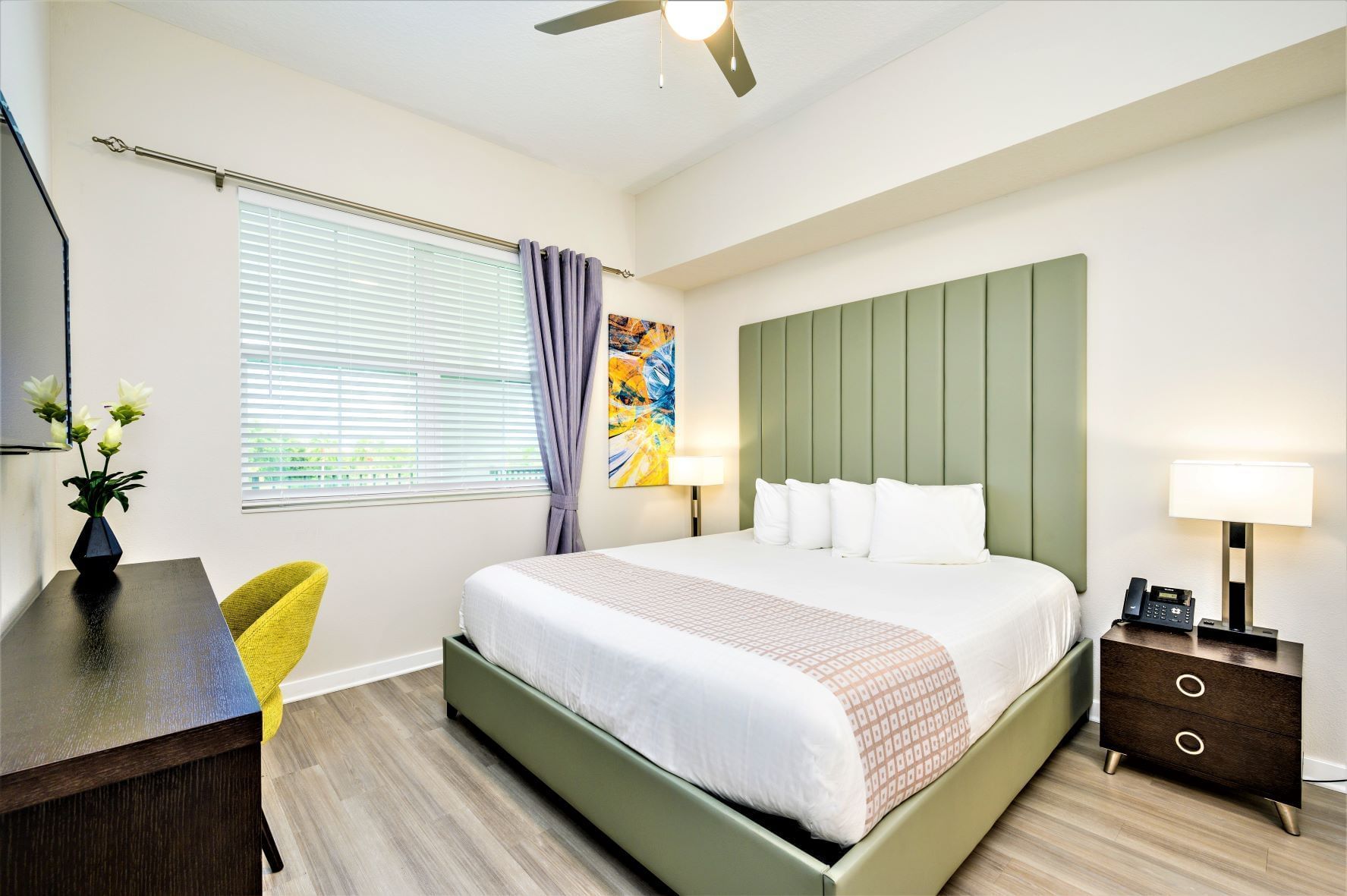 Vista Cay hotel room with a king-size bed, desk, chair, and artwork on the wall near the window.