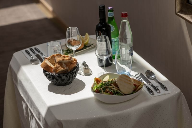 Table setting for one with bread in a basket placed by a salad near wine bottles at Warwick Grand Place Brussels