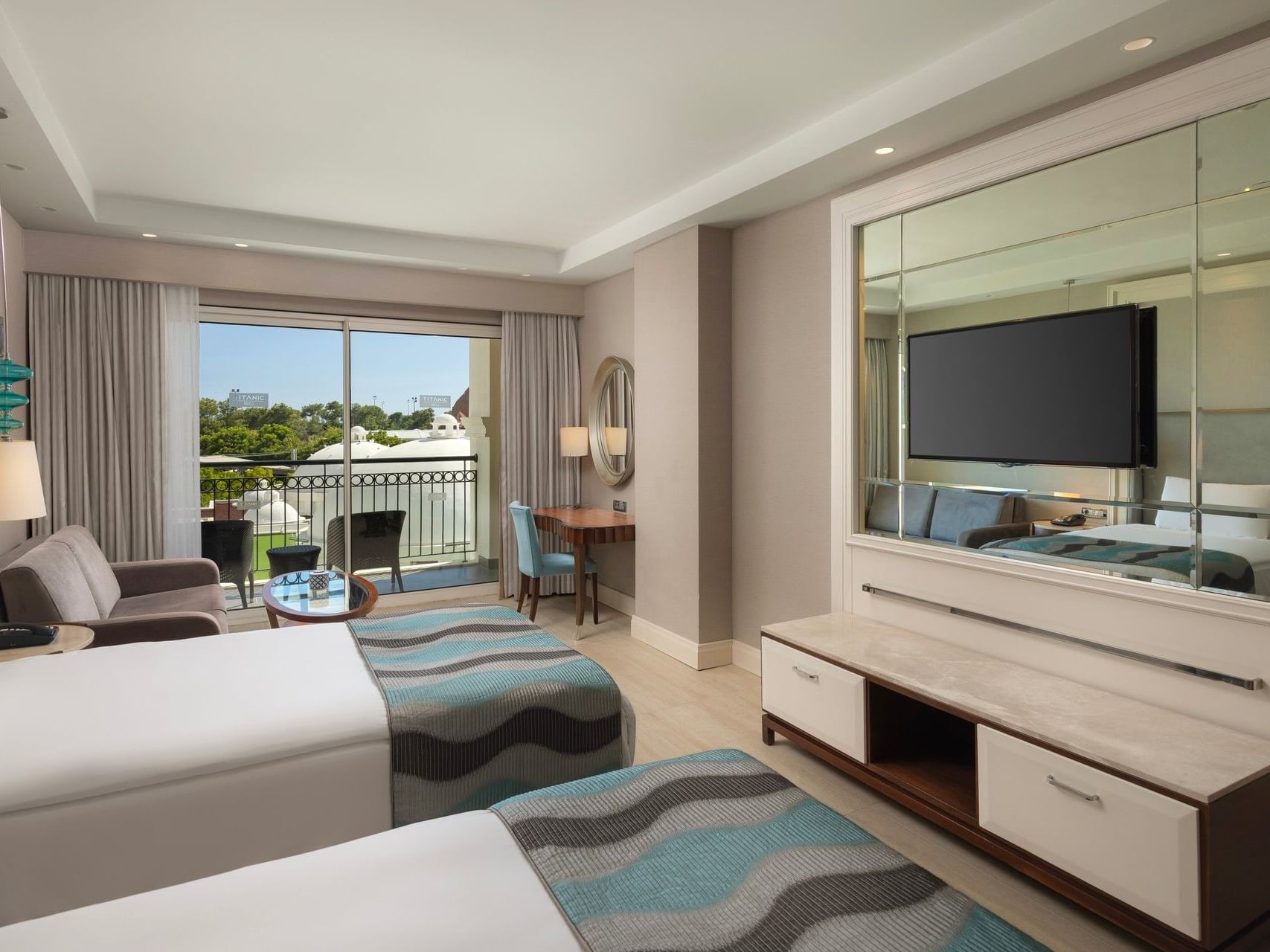 Modern hotel room with twin beds, balcony overlooking golf course, and wall-mounted TV at Titanic Deluxe Golf Belek