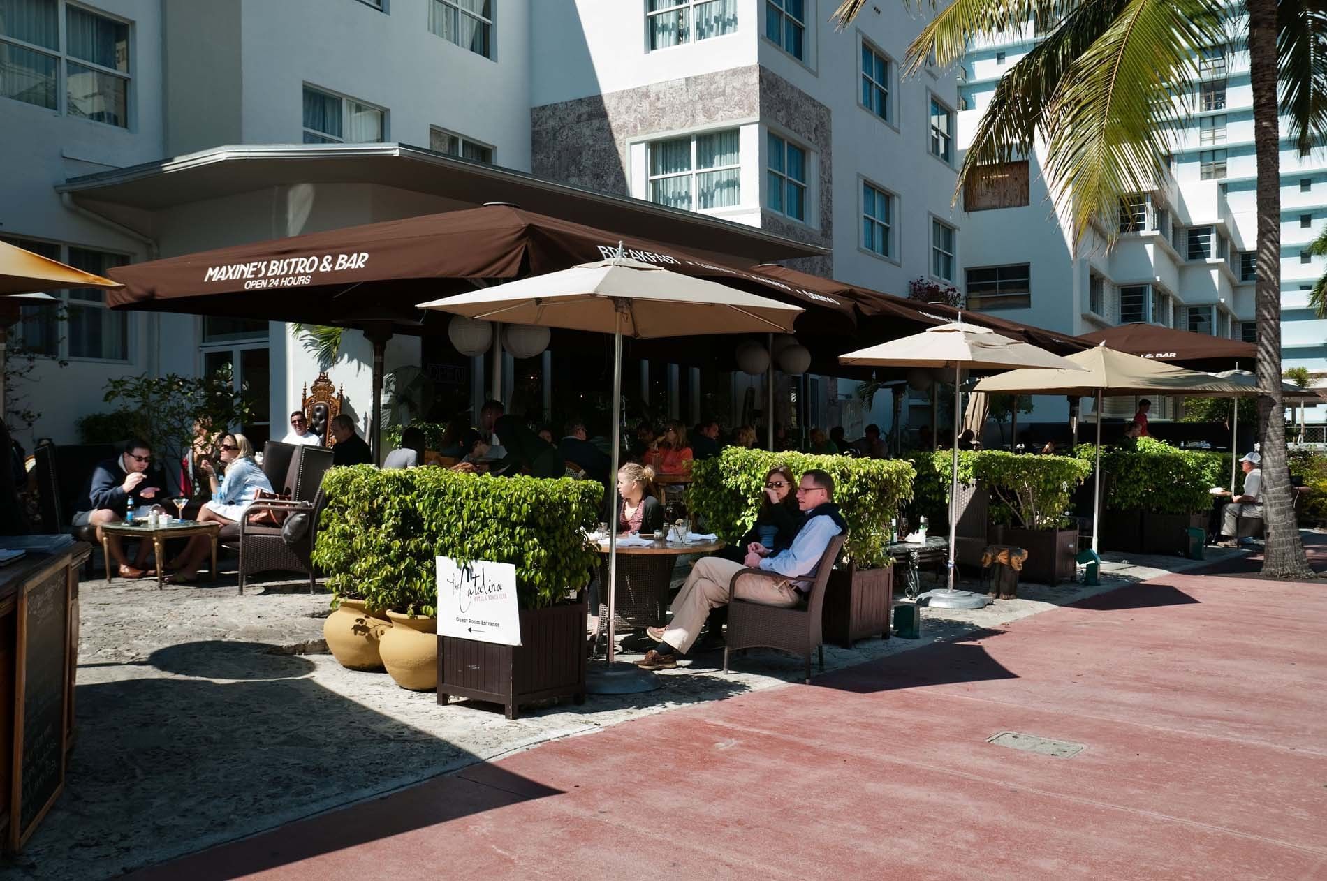 A restaurant patio with outdoor seating, umbrellas, and a brown awning.
