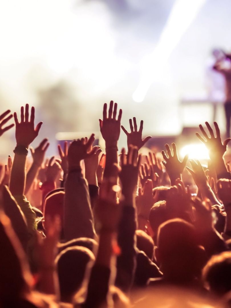 Fans raising hands by a bright stage under glowing spotlights during a show at Warwick Paris Champs Elysées