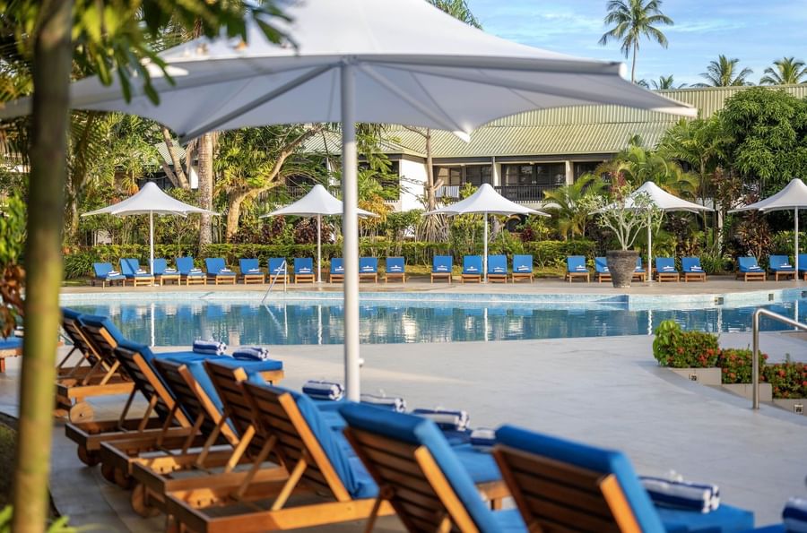 Row of blue sunbeds under white umbrellas by a large pool at The Naviti Resort - Fiji