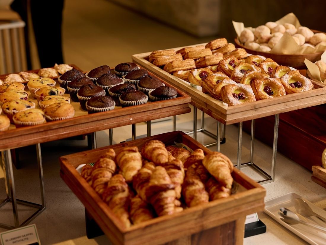 Assorted pastries, muffins, and croissants displayed on wooden trays at The Cliveden buffet breakfast at Pullman East Melbourne
