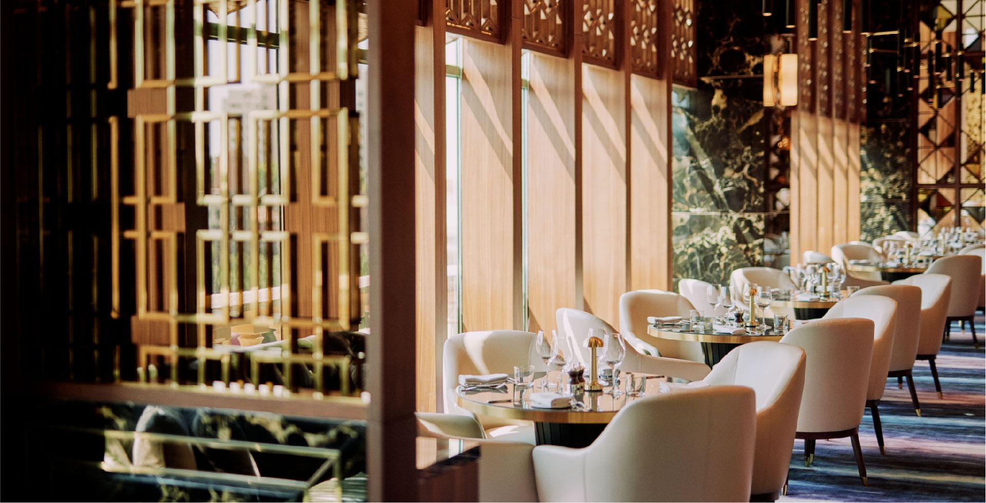 Elegant dining room at Sunway Hotel Pyramid with golden screens, marble accents, and set tables, bathed in natural light