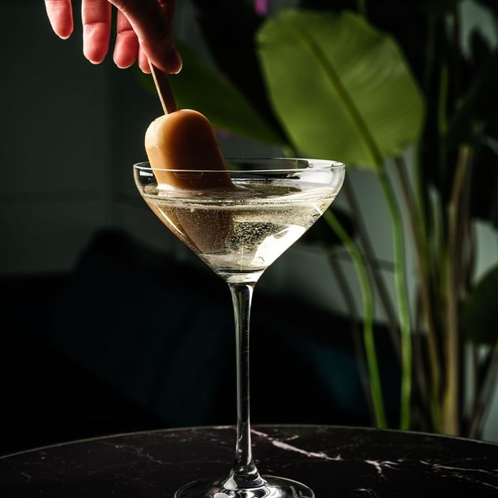 Hand placing a spherical ice cube into a martini glass in The Monkey Bar at Falkensteiner Hotel Prague