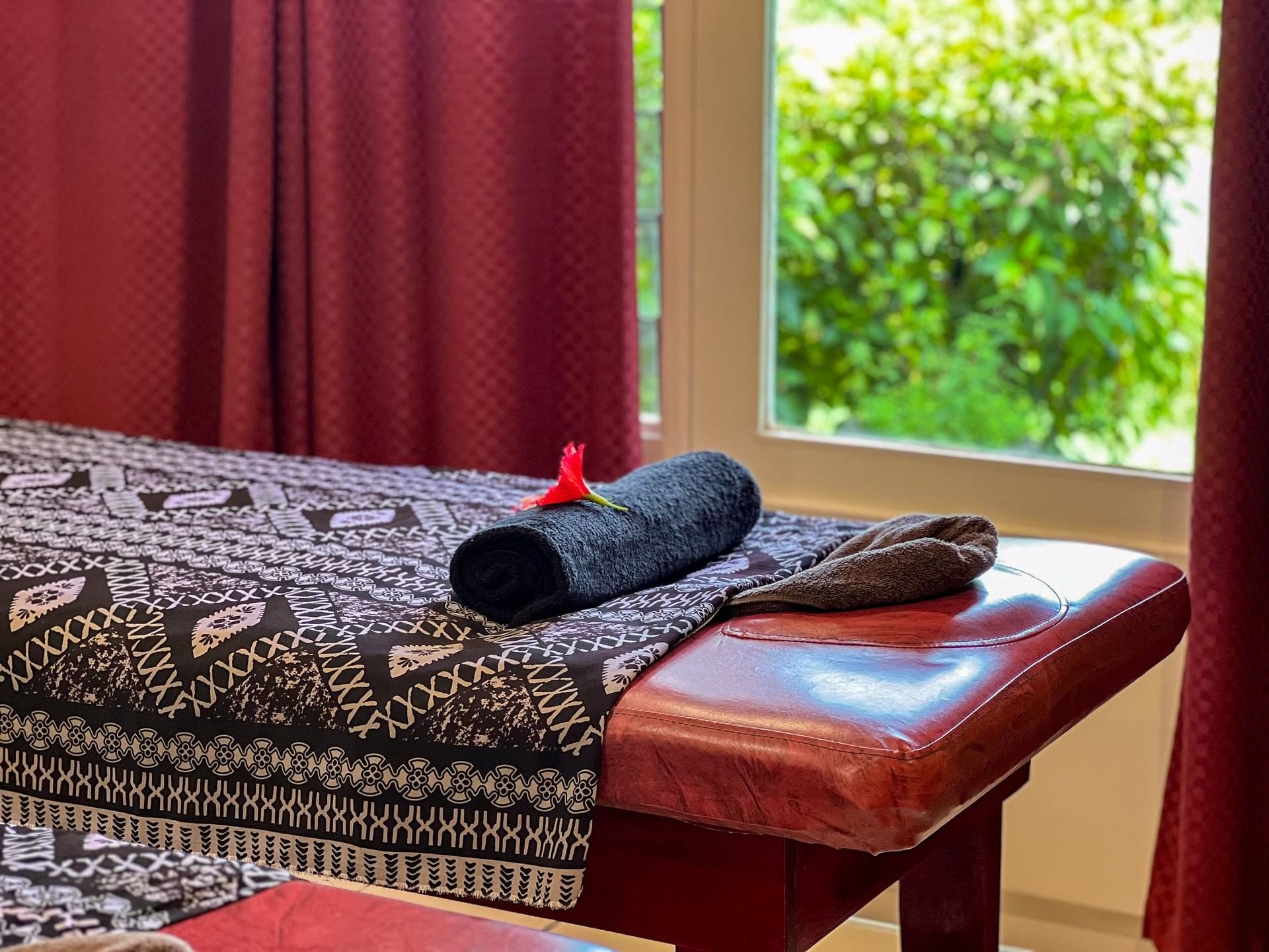 Massage bed with a patterned cover and black towel by a window at TokaToka Resort Nadi Fiji