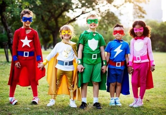 Five young children holding hands and showing off their individual Halloween costumes.