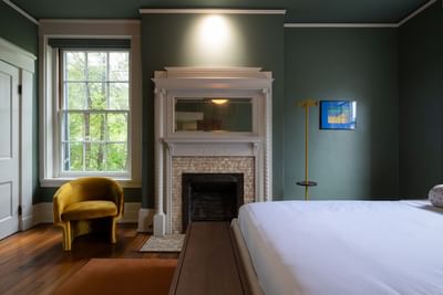 Fireplace and chair by the bed in Luxury Two Queen room at The Ashbrook Hotel, featuring Frankfort Kentucky accomodations