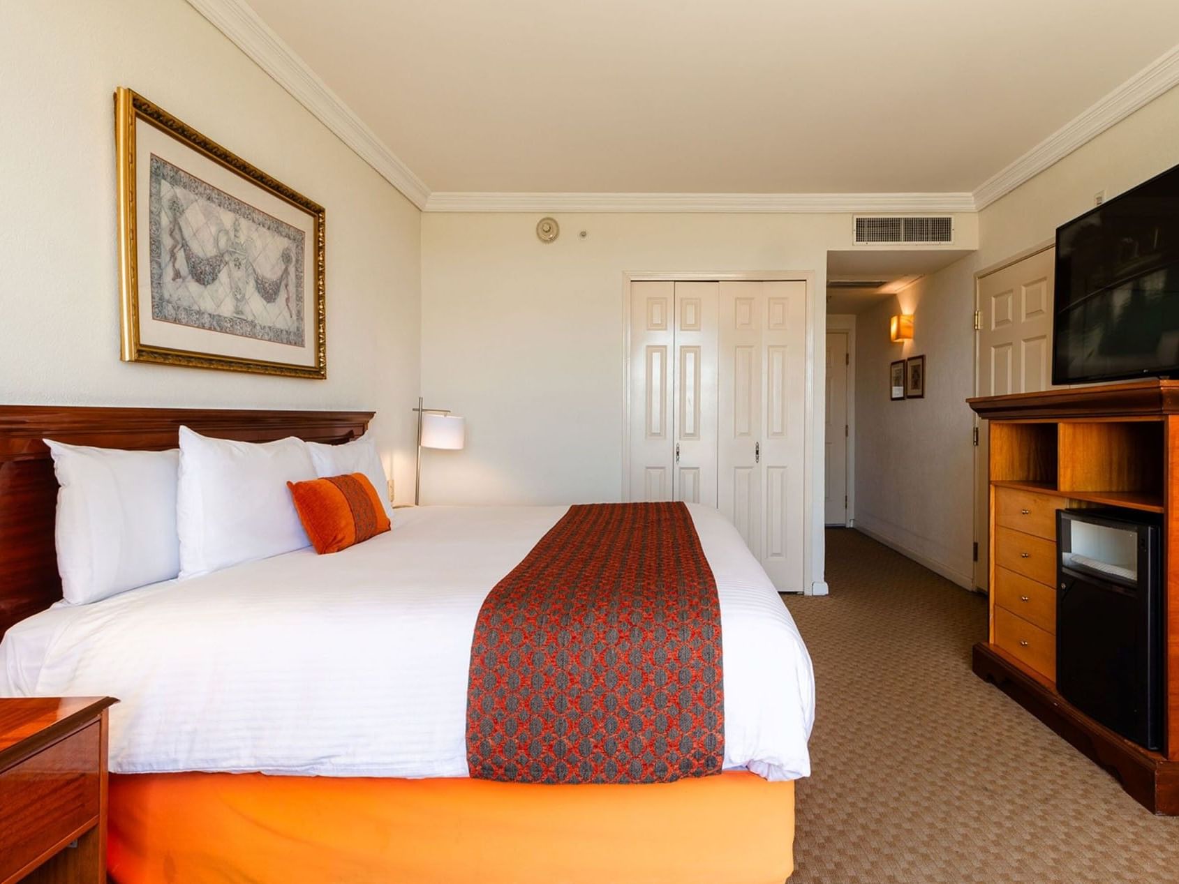 Amplia habitación King Deluxe con consola multimedia de madera y pasillo bien iluminado en Camino Real Puebla Angelopolis