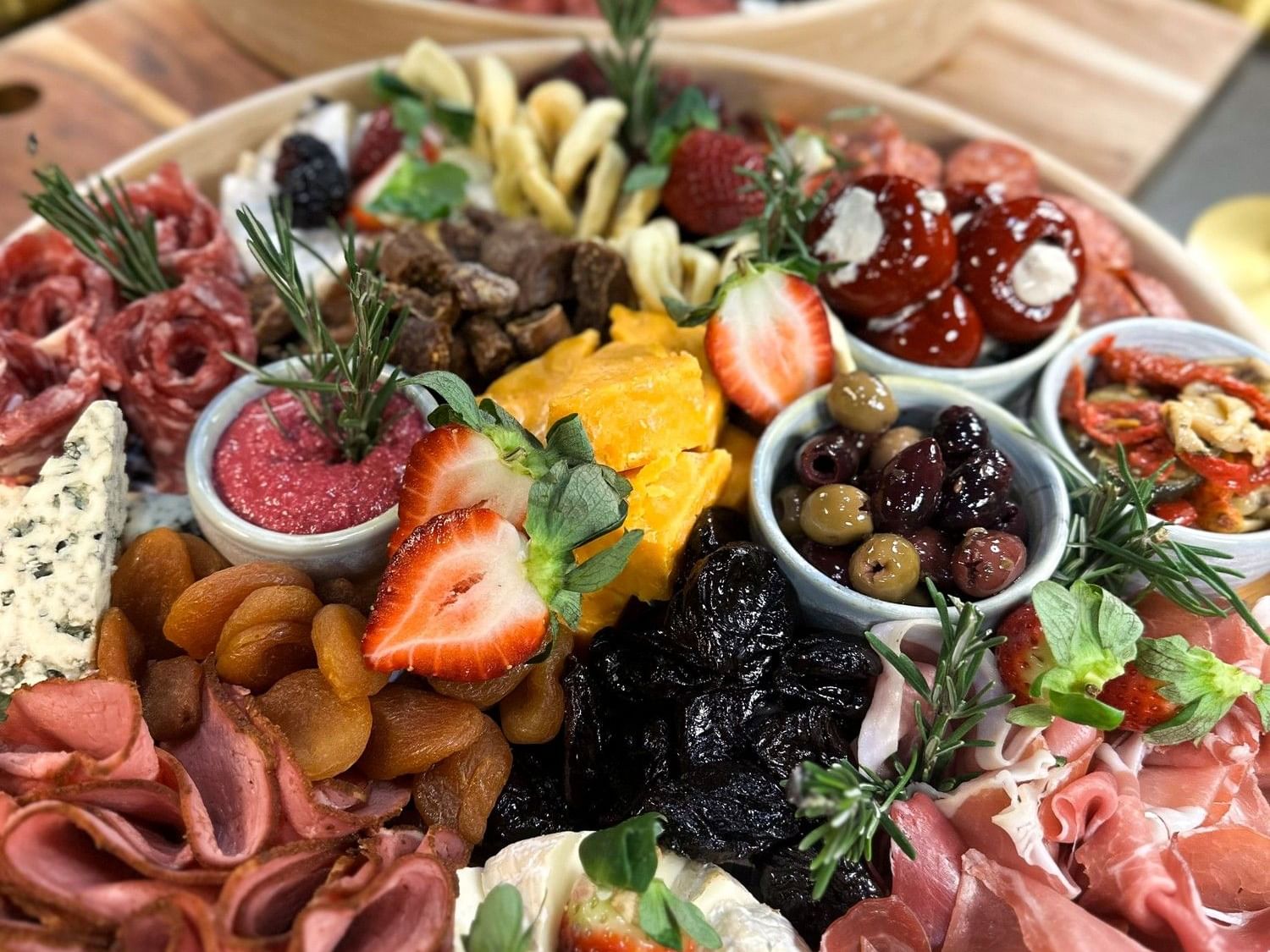 Gourmet charcuterie and cheese grazing platter featuring cured meats, artisan cheeses, olives, dried fruits, fresh berries, dips, and antipasto, beautifully presented for sharing.
