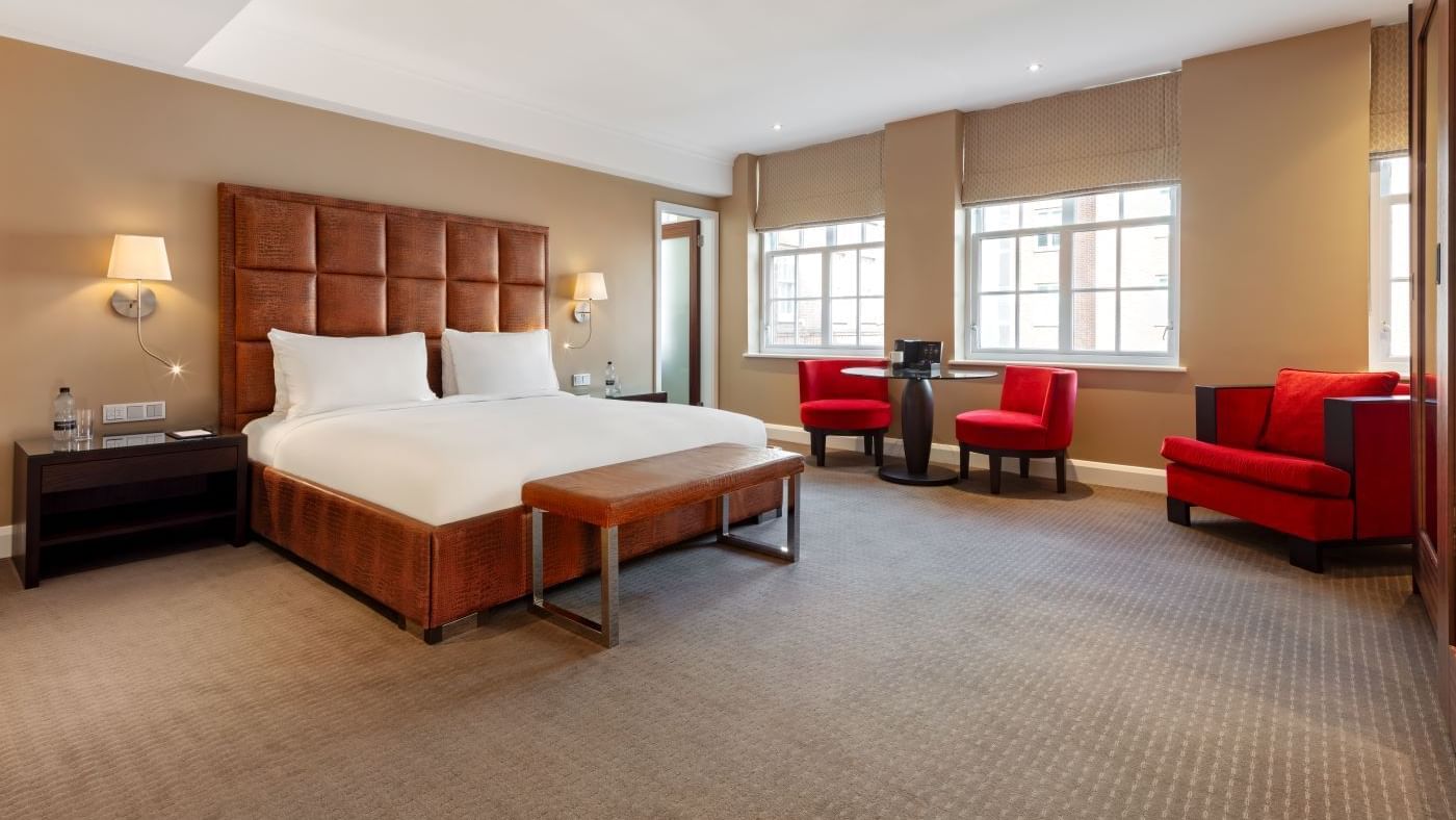 Spacious Collection Deluxe Room at The May Fair Hotel with a king-size bed, red armchairs, and a round table