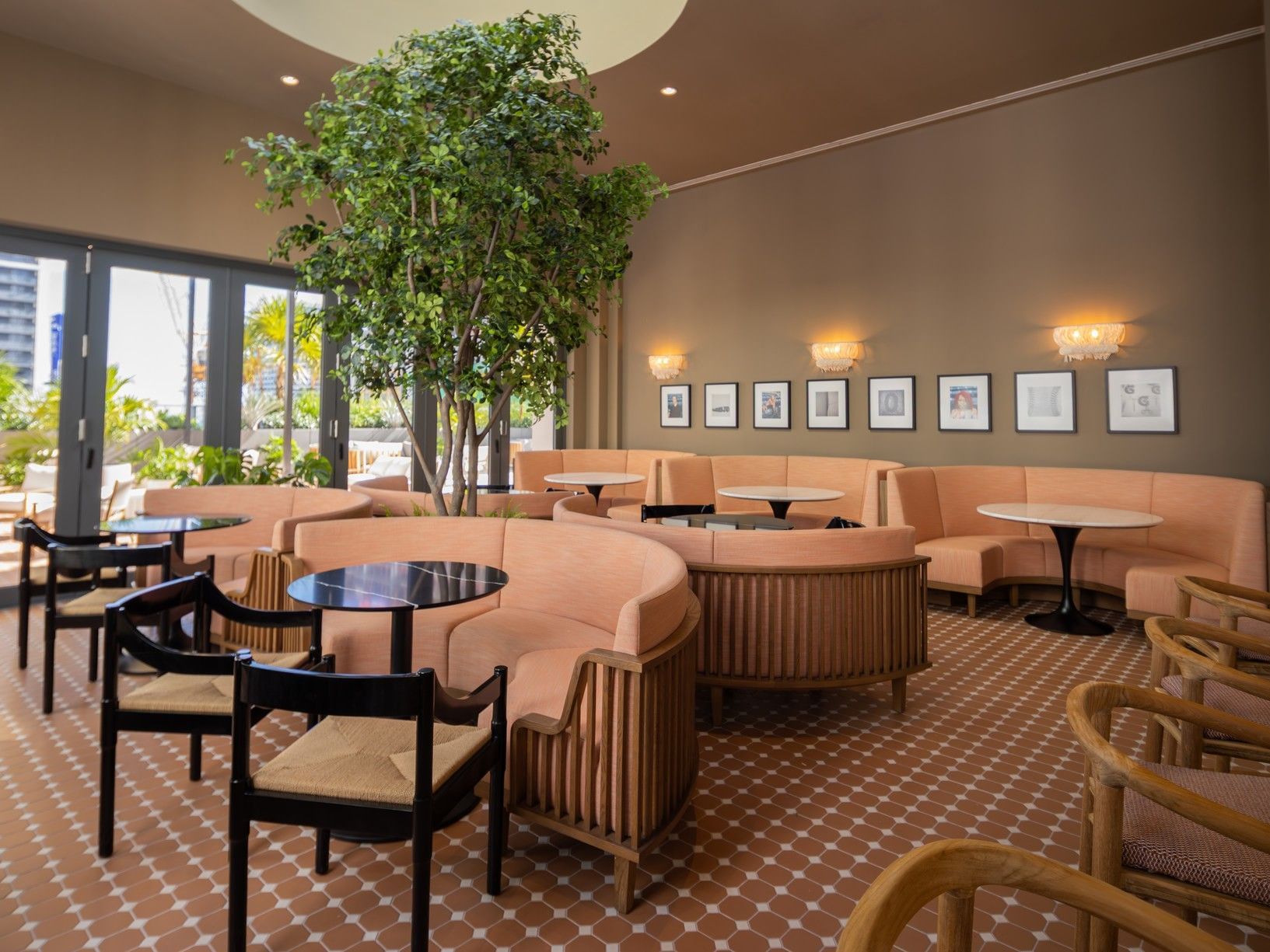Indoor cafe with curved peach booths and a central tree in Private Rooftop Dining and Bar at The Crosby Miami World Center