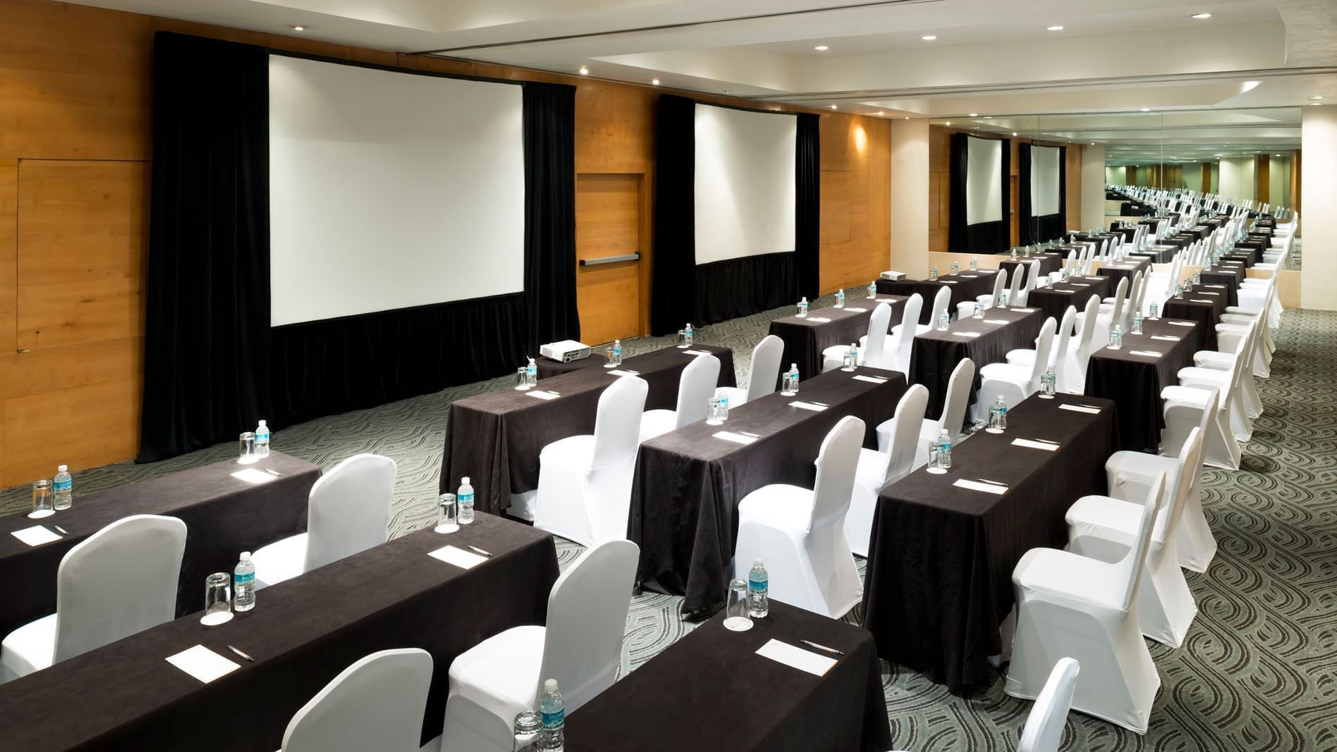 Theater-style Nueva York Venue with rows of desks, white chairs, and wall mirrors at Real Inn Perinorte