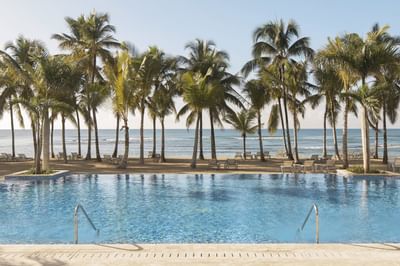 Outdoor pool by the beach with coconut trees at Club Hemingway