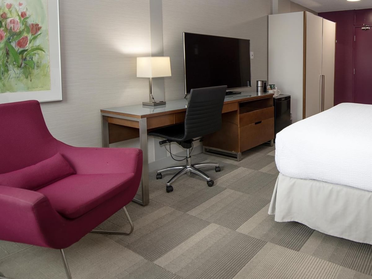 Coast Queen room with work desk, pink accent chair, flat-screen TV, and white bed at Coast Prince George Hotel