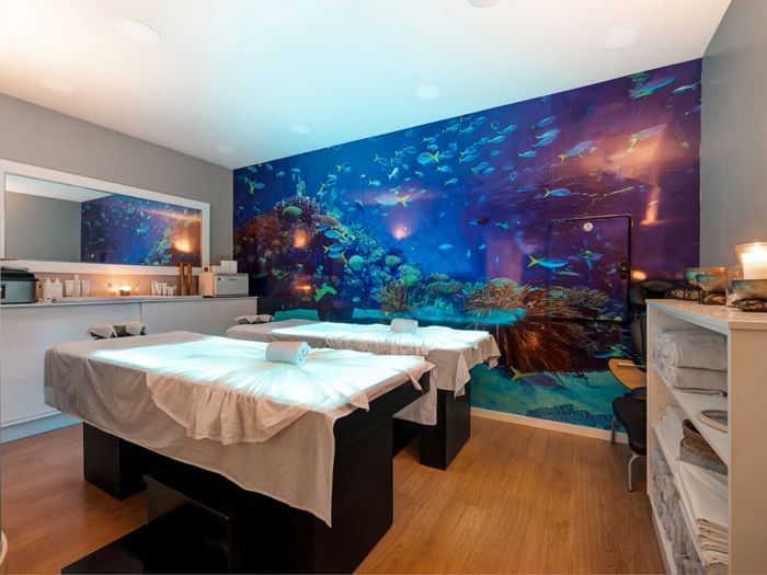 The tranquil couples spa room at Hotel Do Caracol, featuring glowing massage tables and an aquatic mural