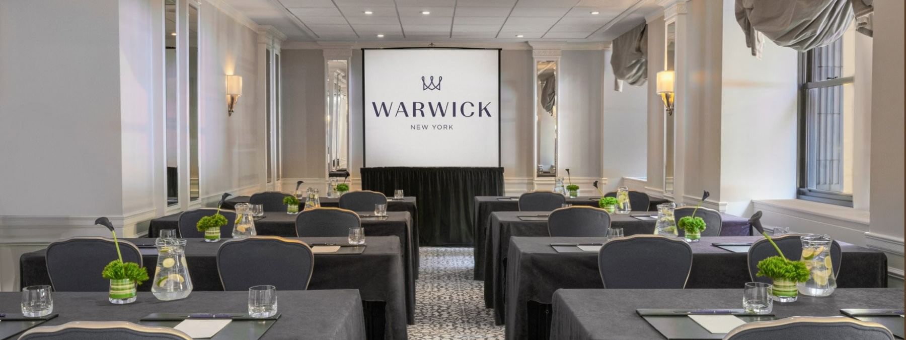 Essex Classroom table set-up facing large screen with glasses & green floral arrangements at Warwick New York