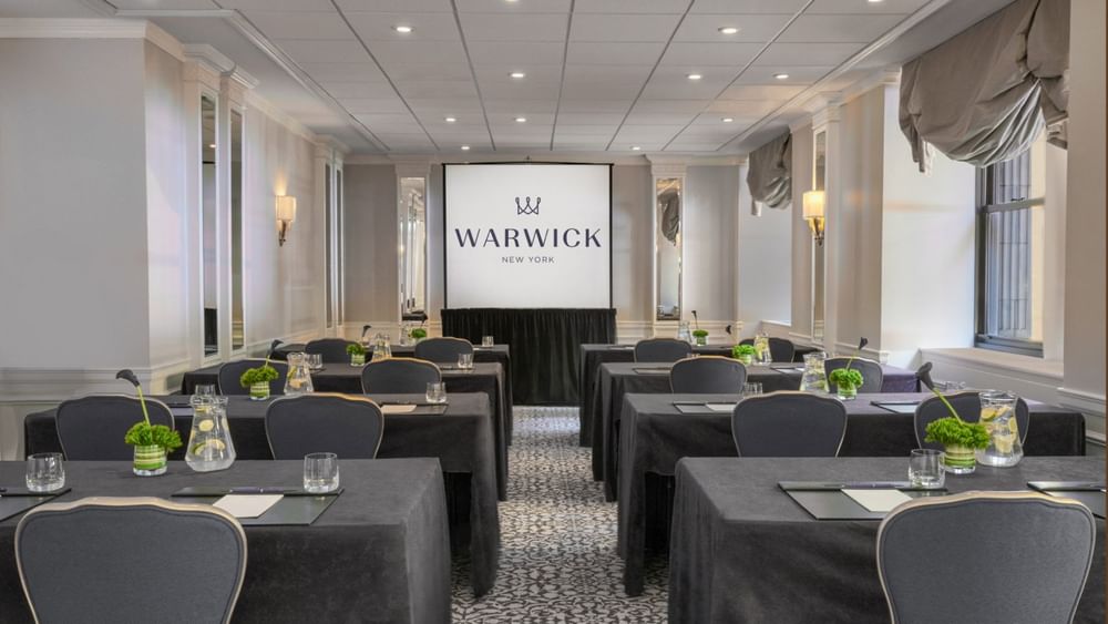 Essex Classroom table set-up facing large screen with glasses & green floral arrangements at Warwick New York