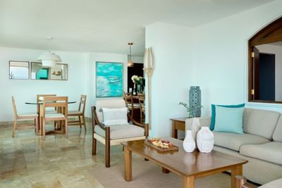 Living room with sofa, coffee table, armchair, dining table, and artwork on the wall.