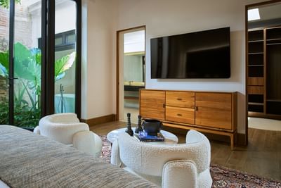 Casa Campanas bedroom with two armchairs, a TV, a wooden cabinet, and a view of a garden at Singular Signature Residences