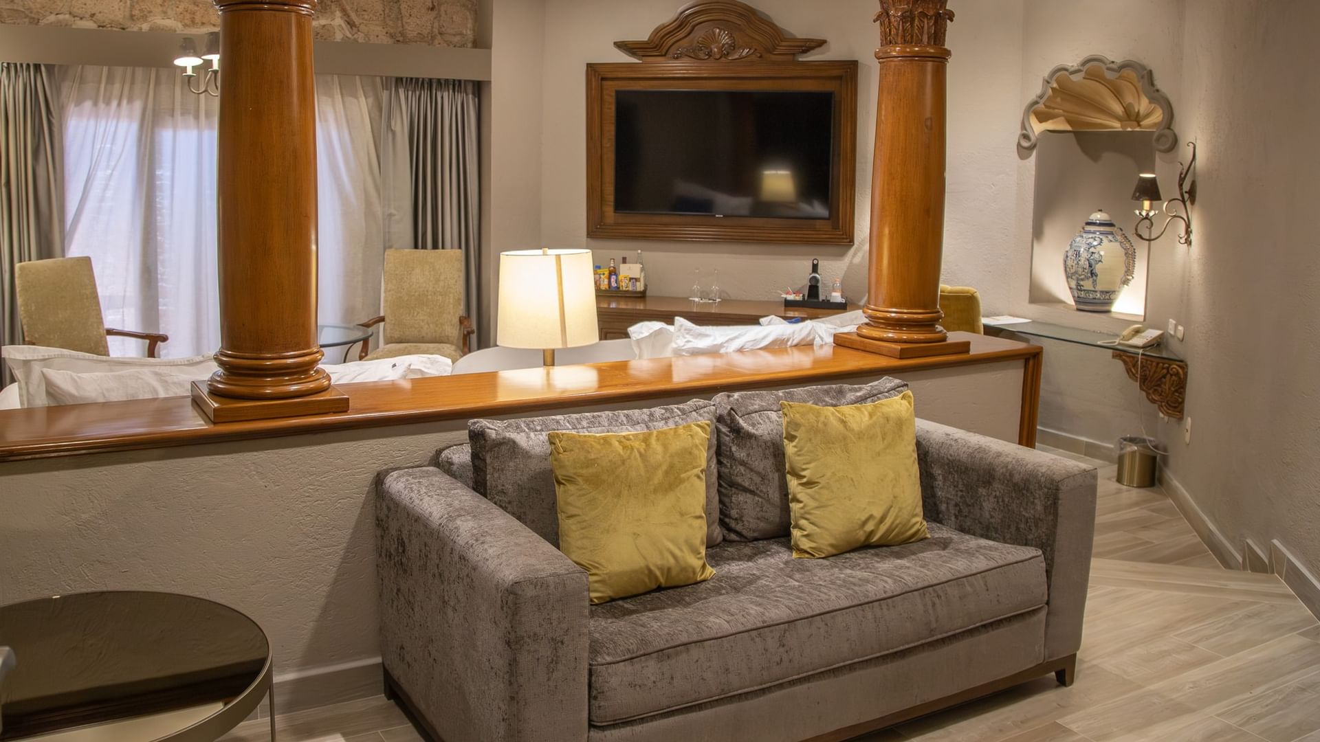 Spacious room with gray sofa, yellow pillows, wooden columns, and two double beds at Quinta Real Guadalajara