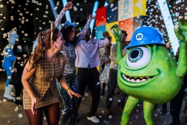 One-eyed green monster Mike Wazowski dances with a group of adults in snowfall during the Pixar Dance Party at Jollywood Nights. 