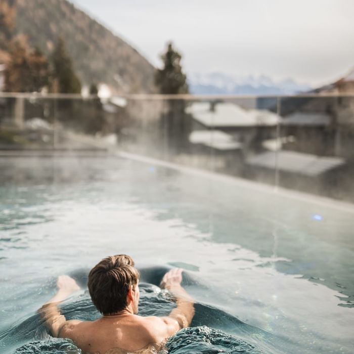Man floating in outdoor pool with mountain view at Falkensteiner Hotel Falkensteinerhof