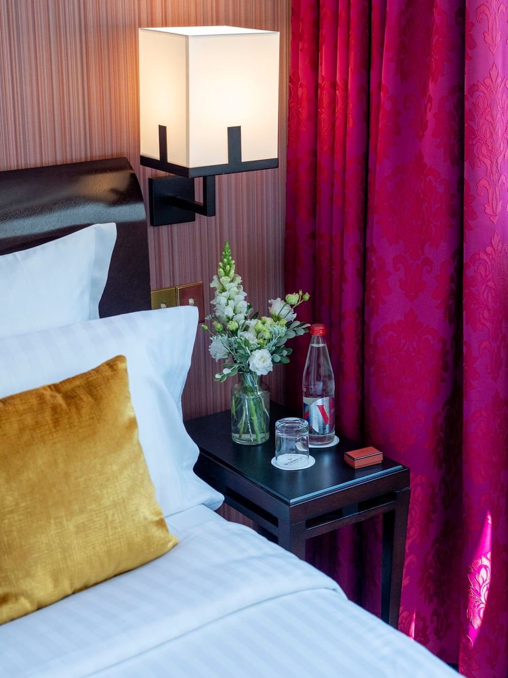 White flowers in a vase by a water bottle on a black side table in Elegant Deluxe at Warwick Paris Champs Elysées