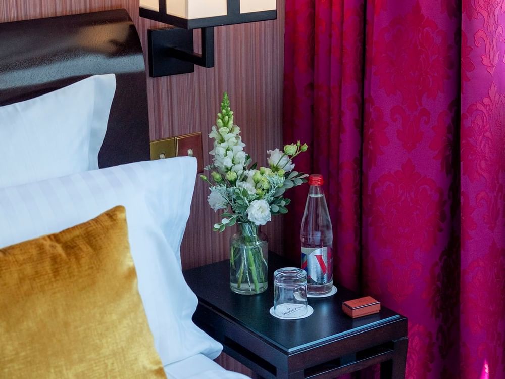 White flowers in a vase by a water bottle on a black side table in Elegant Deluxe at Warwick Paris Champs Elysées