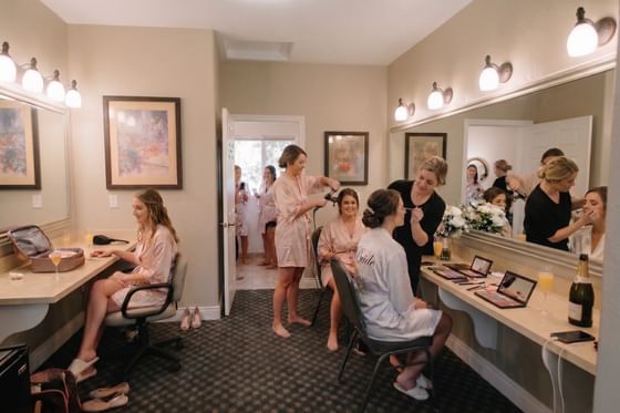 Bride getting ready by a long vanity mirror under bright wall lights at the Oregon Garden Resort
