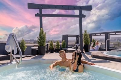 A couple relaxing in a rooftop hot tub with a breathtaking city view at Acclaim Hotel Calgary