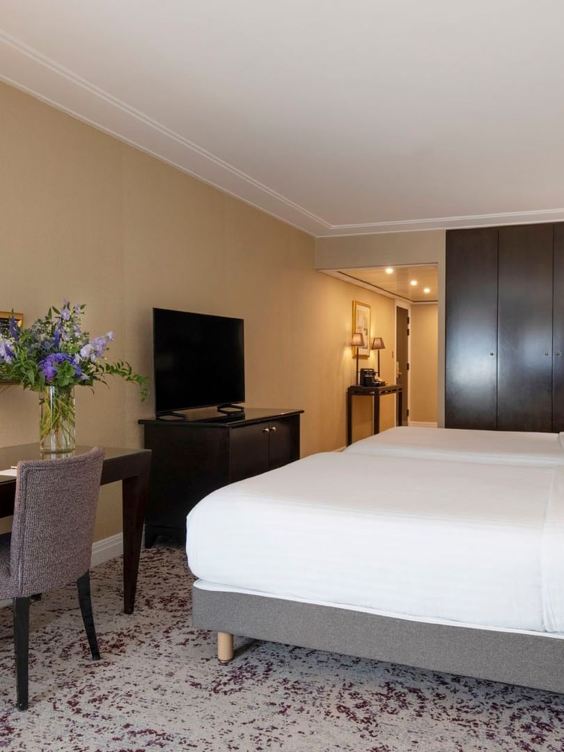 Twin beds by a dark wooden desk under gold mirrors in Family room with two queen beds at Warwick Paris Champs Elysées