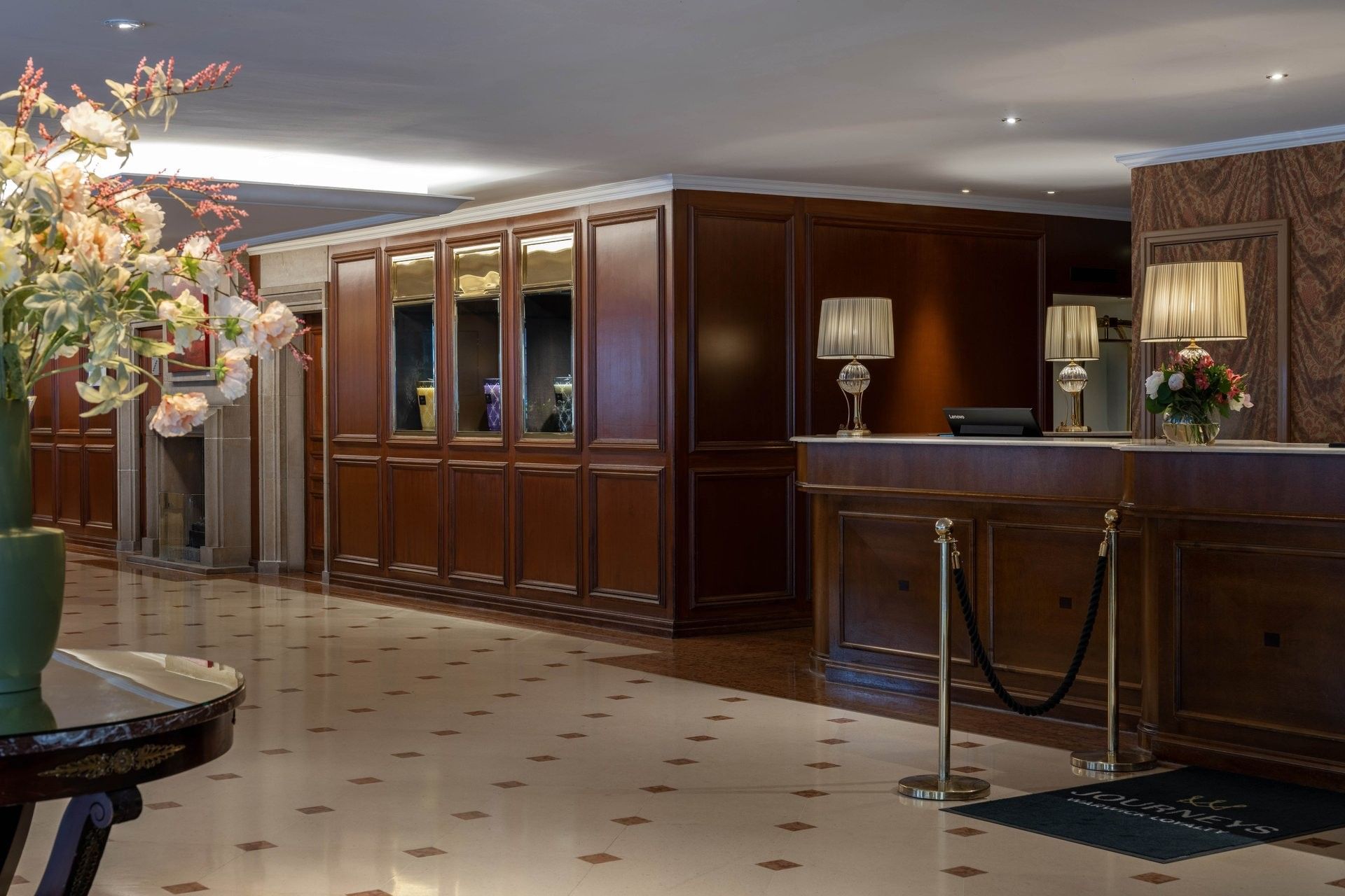 Lobby with lamps placed by dark wood reception desks under soft ceiling lighting at Warwick Grand Place Brussels