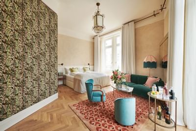 Spacious Junior Suite at Hotel Motto Vienna, featuring a comfortable bed, a green sofa, and an elegant chandelier