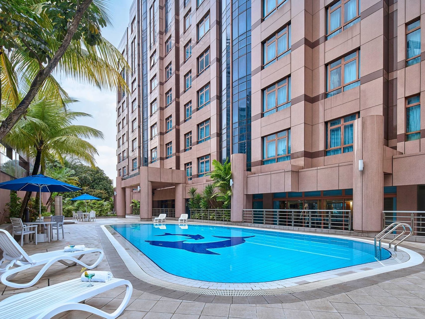 Serene Orchard Grand Court pool area with lounge chairs, umbrellas, and lush palms beside a modern building