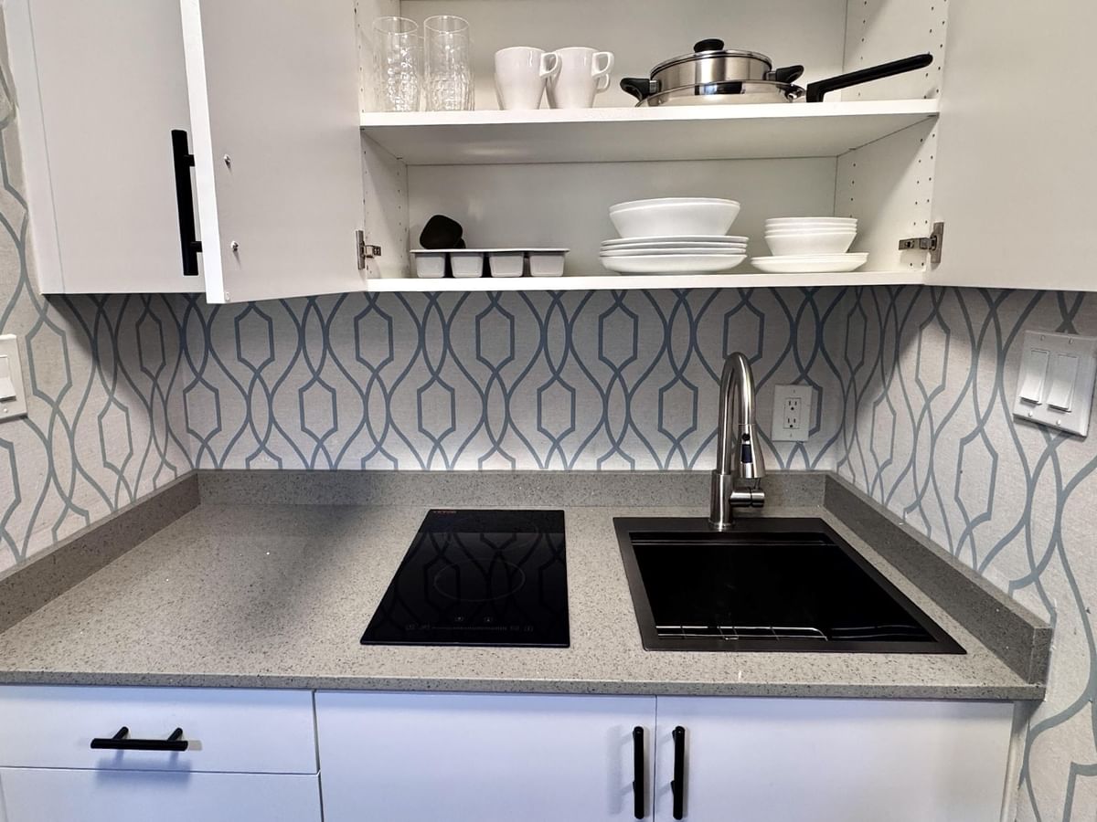 White kitchen with induction cooktop, sink, wall-mounted cabinets, and geometric wallpaper on the wall.