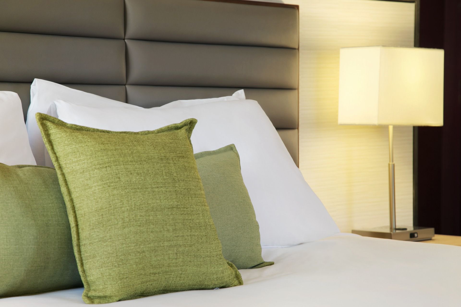 Green pillows on bed with white sheets next to lamp