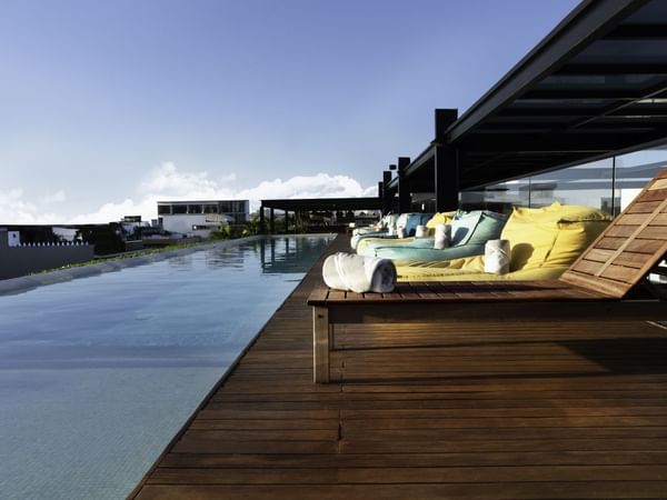 Spectacular rooftop infinity pool at Fiesta Inn Playa del Carmen featuring wooden loungers under a bright blue sky