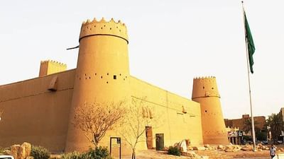 Masmak Citadel with circular towers by a flag and desert plants near Cantonal Hotel by Warwick Riyadh