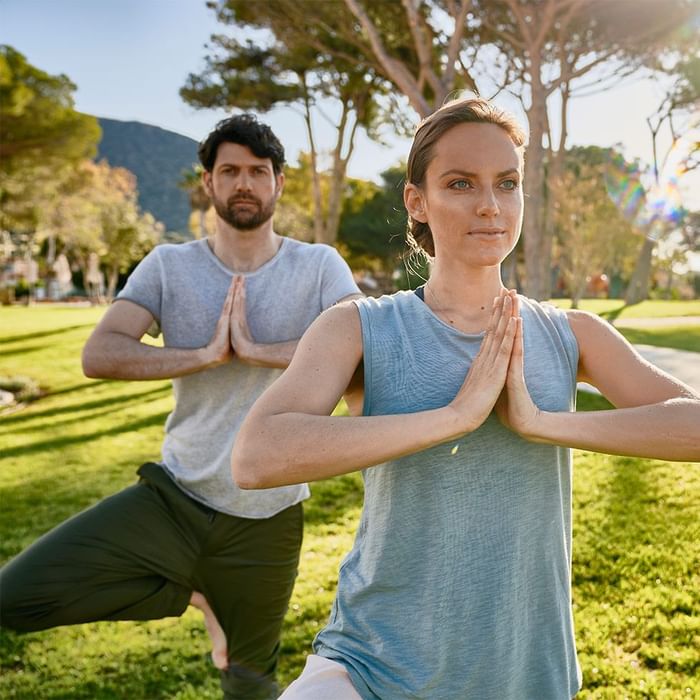 Two people practicing yoga on a green lawn near Falkensteiner Resort Capo Boi